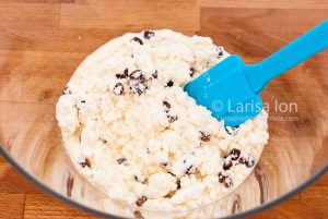 Mixed pastry for syrniki in a glass bowl with a silicone spatula closeup.