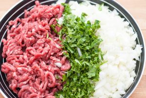 Raw minced meat with finely chopped fresh greens and onion in a bowl closeup.