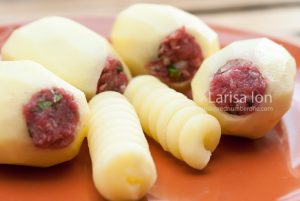 Raw potatoes stuffed with minced meat on a brown plate closeup.
