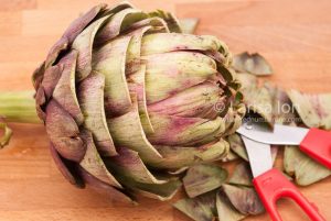 Artichoke with scissors on a wooden cutting board closeup