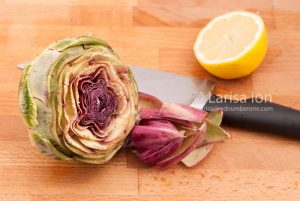Raw artichoke and lemon with a knife on a wooden cutting board c